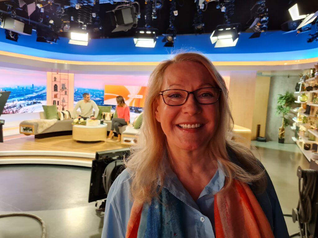 Barbara lächelt happy in die Fotokamera. Das Intervie ist vorbei, im Hintergrund arbeiten die moderatorinnen im Puls 4 Studio weiter.