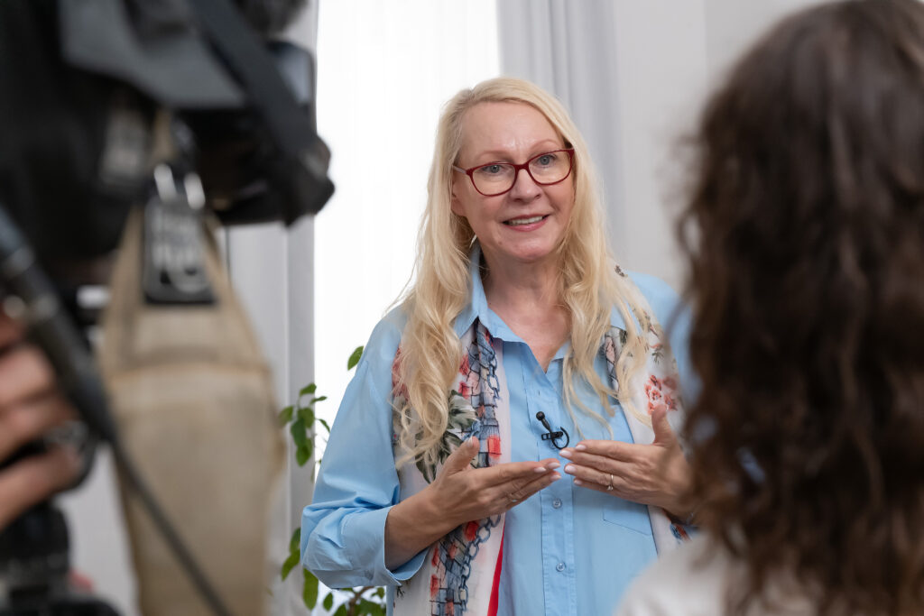 Barbara beim Interview, mit leicht gestikulierenden Händen. Von der ORF Redakteurin sieht man nur den Hinterkopf.